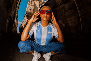 Person wearing a blue and white sports jersey with red sunglasses sitting on steps.