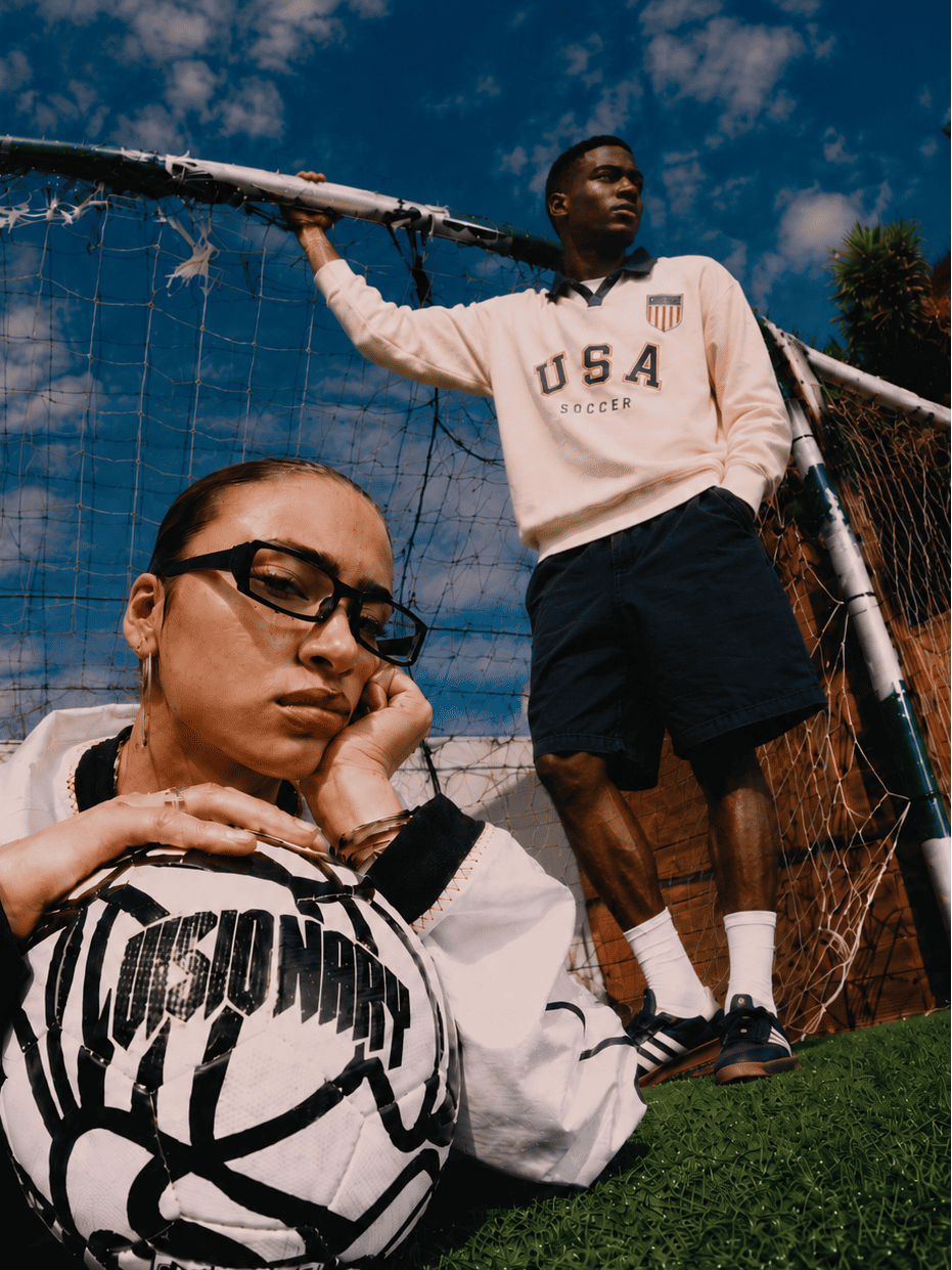 Two people on a soccer field with a soccer ball, one wearing a 'USA Soccer' sweatshirt.