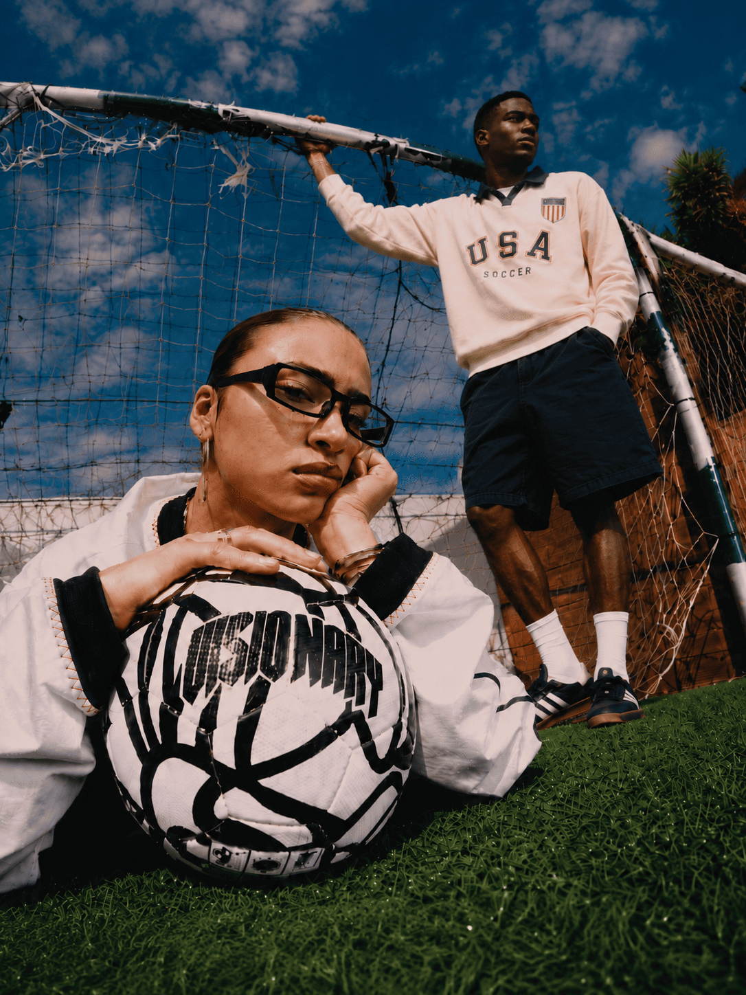 Two people on a soccer field with a soccer ball, one wearing a 'USA Soccer' sweatshirt.