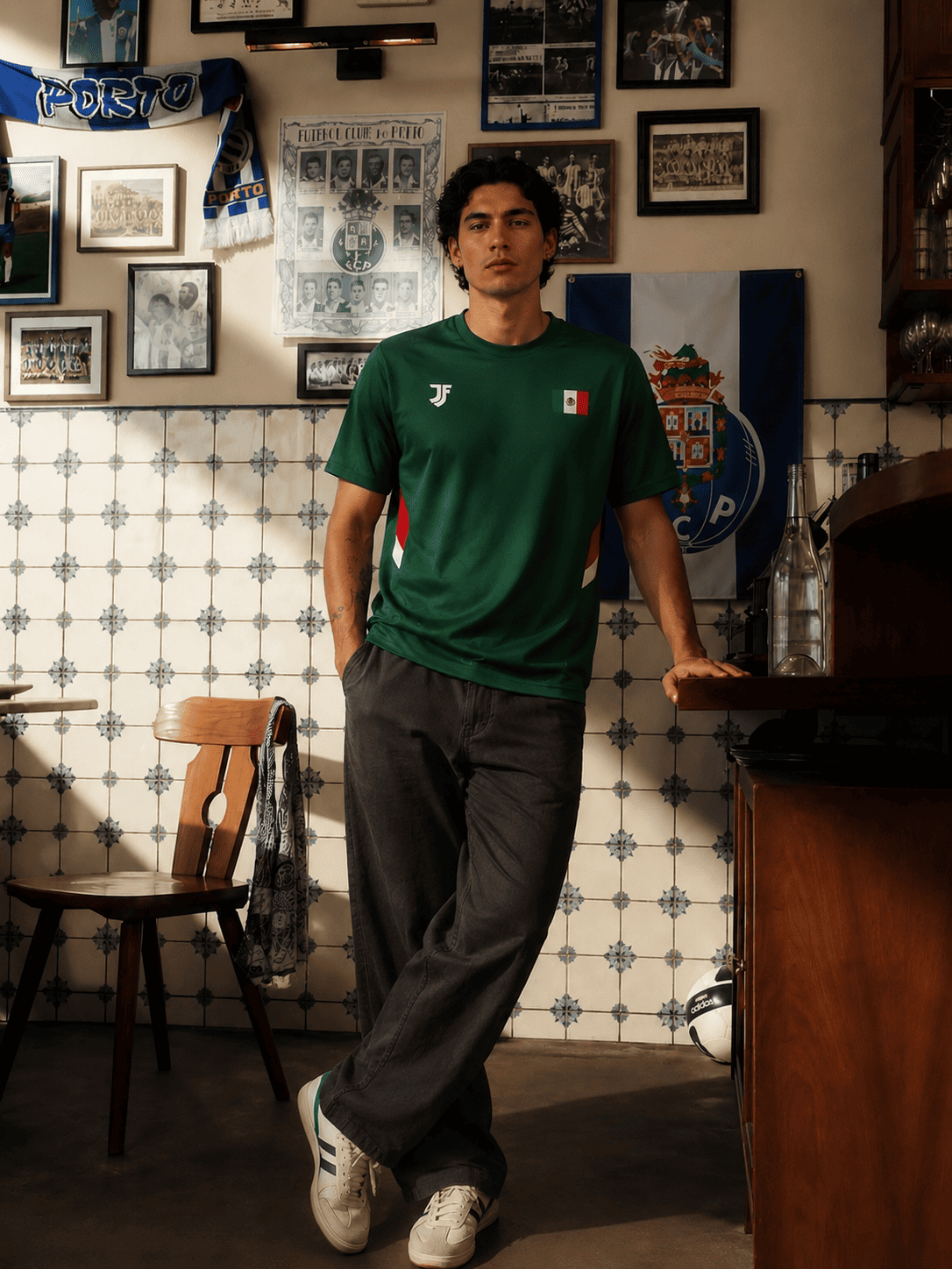 Man wearing a green t-shirt with a logo in a room with tiled walls and framed pictures.